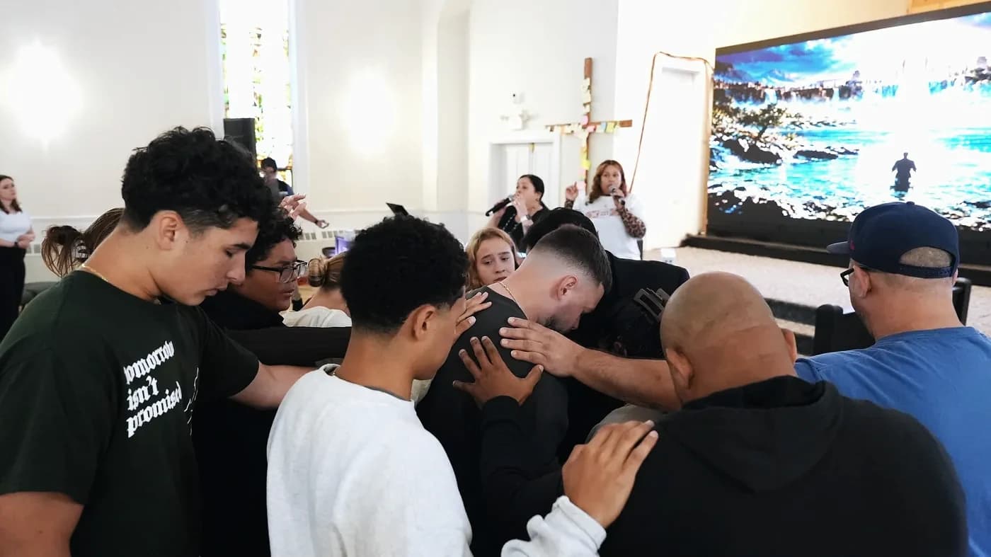 Young people and leaders praying over a young man while the worship team sings
