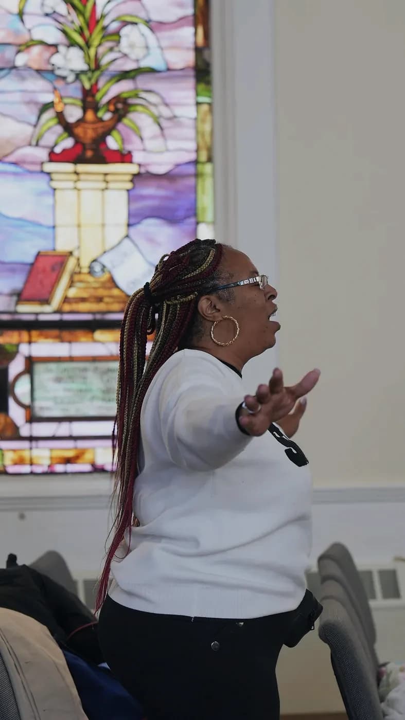 A woman worships with open arms in front of a stained glass window